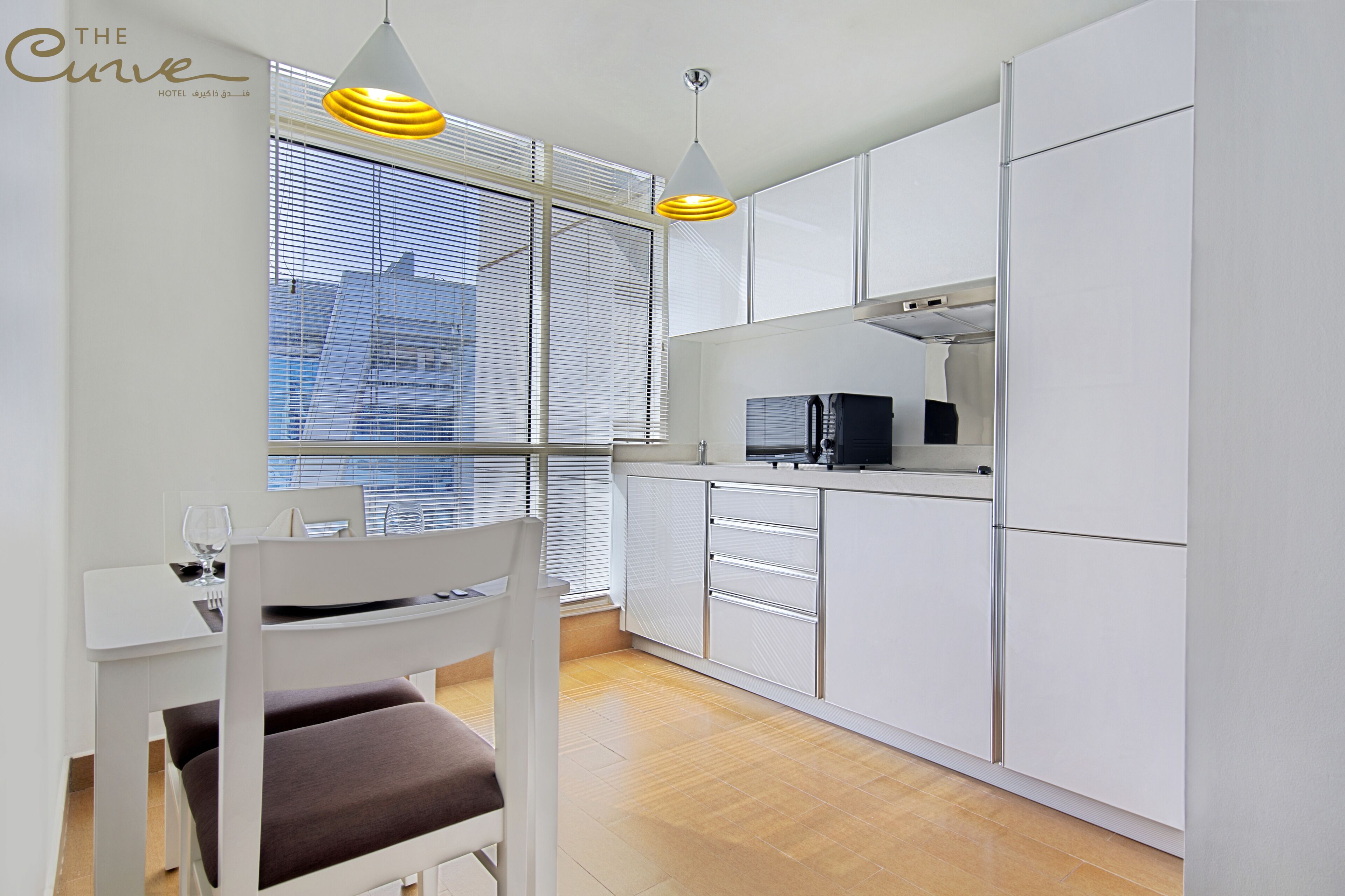 Eine moderne Küche mit weißen Schränken, einem Esstisch mit einem Stuhl und Blick auf die Stadt durch große Fenster.