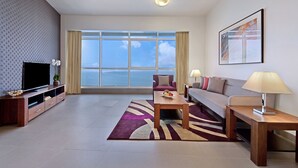 Una habitación de hotel moderna con un ventanal grande, un televisor de pantalla plana, un sofá, una mesita de café y una lámpara.