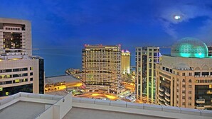 Un paisaje urbano nocturno con edificios altos, una estructura en forma de cúpula y vista al mar.