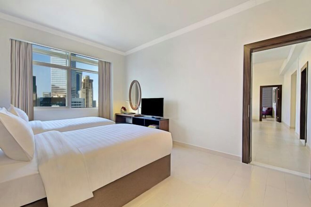 Una habitación de hotel moderna con dos camas, un ventanal grande, un televisor de pantalla plana y un espejo.