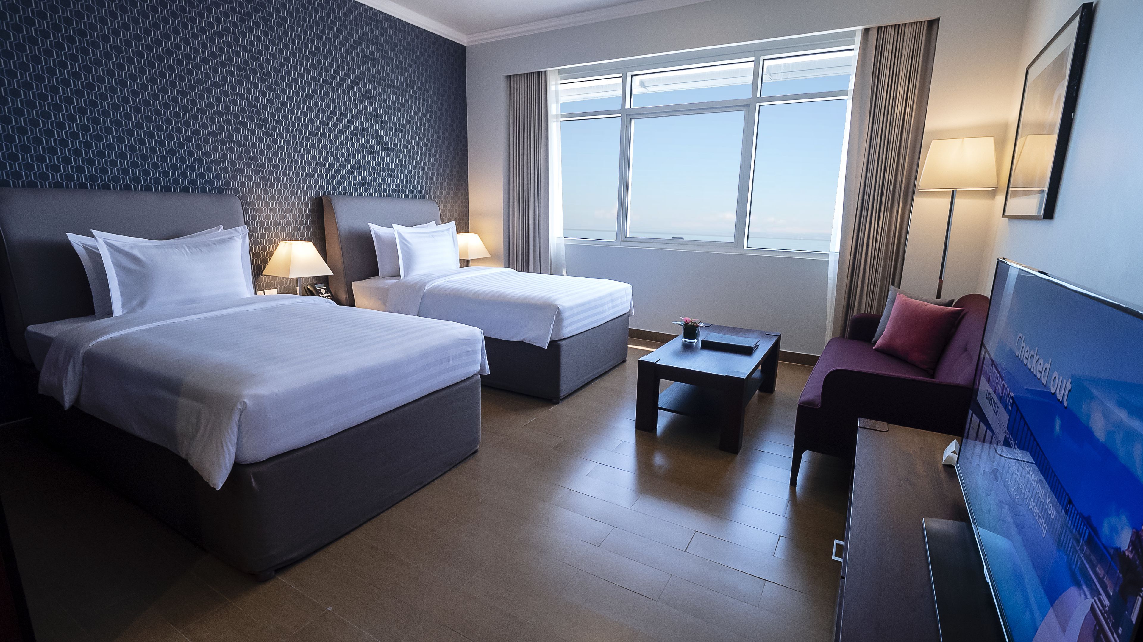 Habitación de hotel con dos camas, un escritorio, una silla y un ventanal grande.
