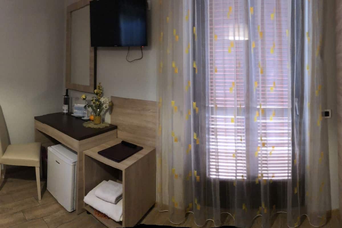 A hotel room with a bed, a desk, a chair, a small fridge, a TV, and a bathroom.