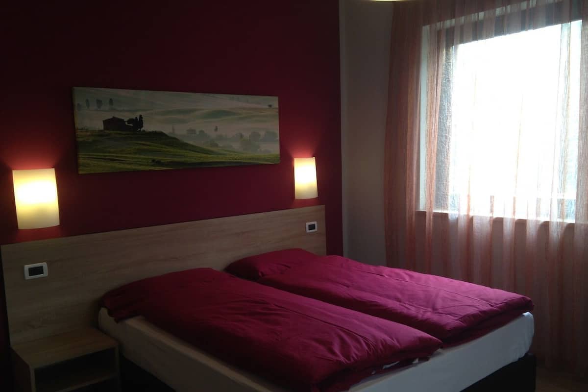 A hotel room with a bed, two bedside tables, a wall-mounted painting, and two wall-mounted lamps.