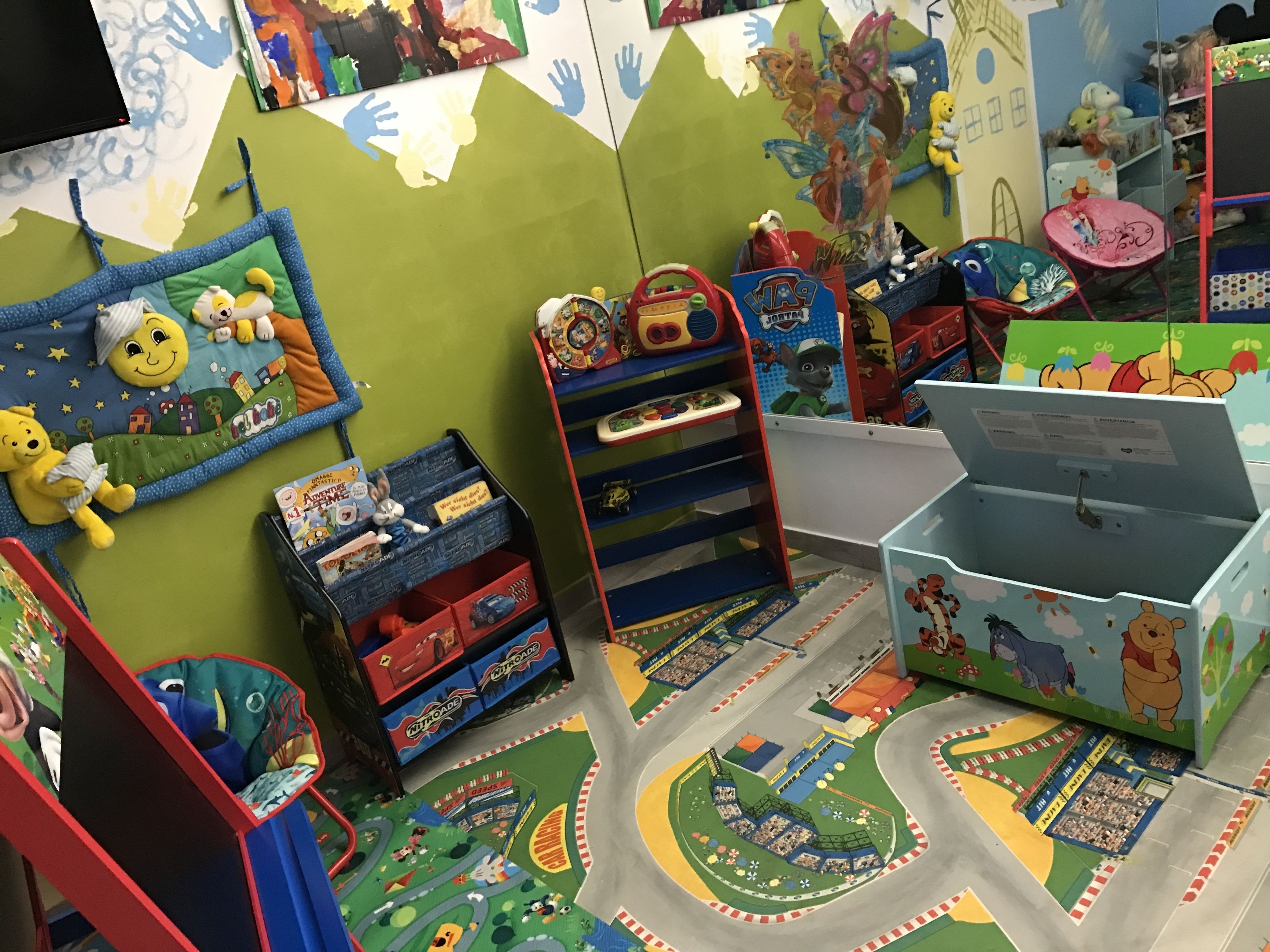 A child's playroom with a colorful play mat, toy storage units, and a shelf with plush toys.