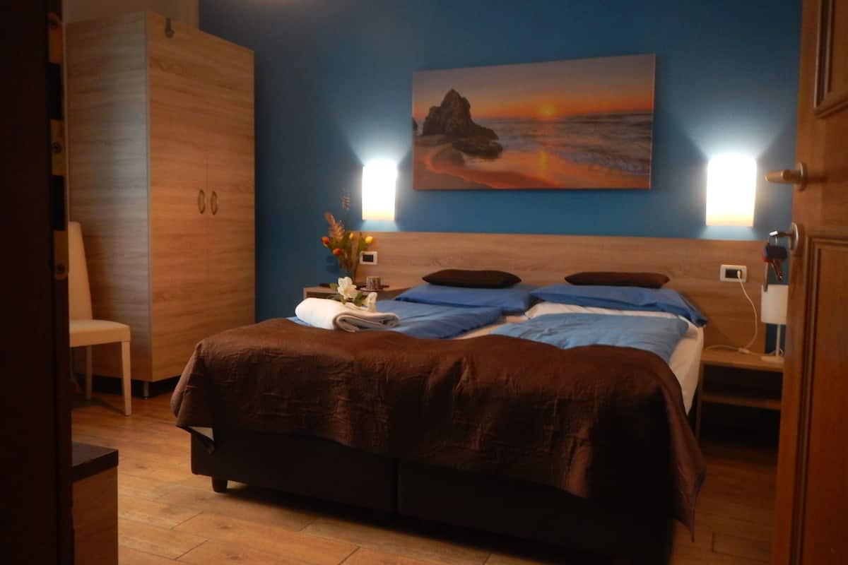 A bedroom with a bed, a nightstand, a chair, and a painting on the wall.