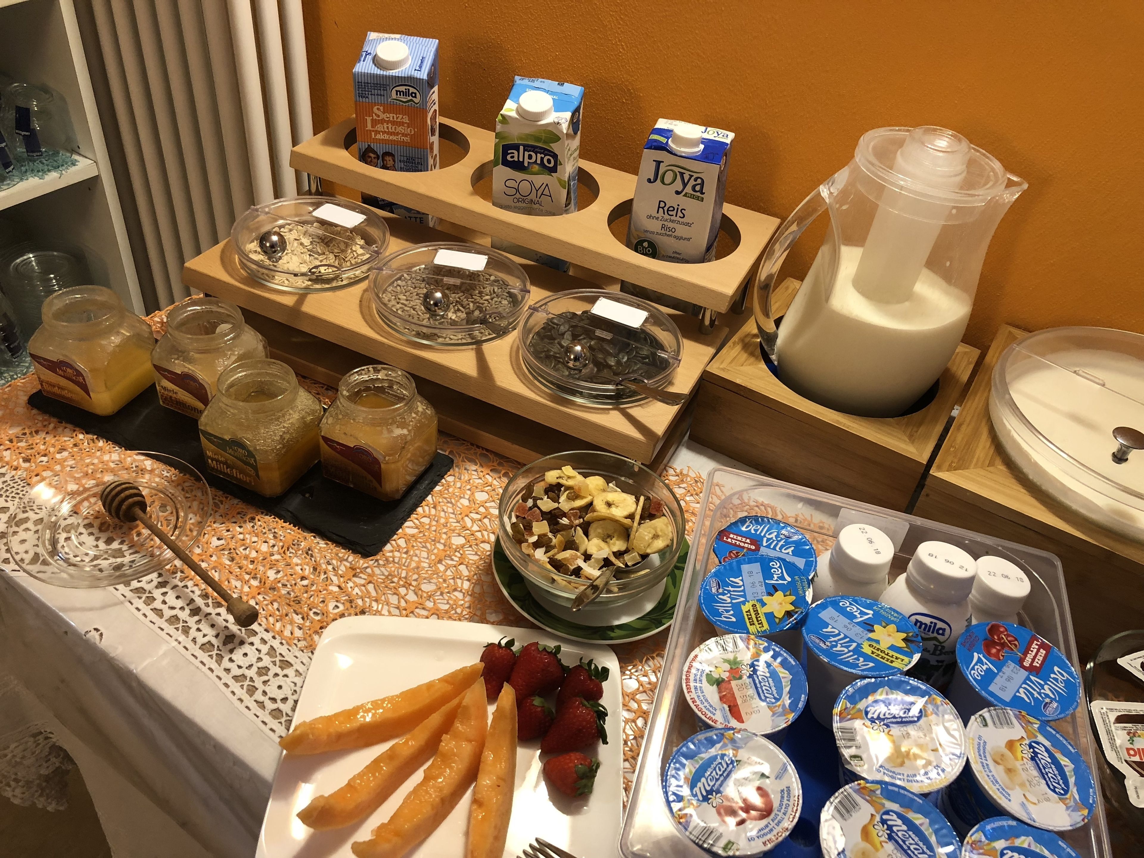 Un buffet con diversi cibi e bevande, tra cui barattoli di conserve, una ciotola di frutta secca e vasetti di yogurt.