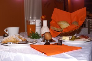Aamiaispöytä, jossa on croissantteja, leipäkori, juustoa ja suolakurkkuja.