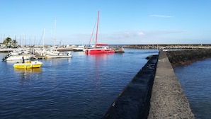 En lysthavn med forskellige både i havnen, en rød sejlbåd i fokus, og et roligt hav under en klar himmel.