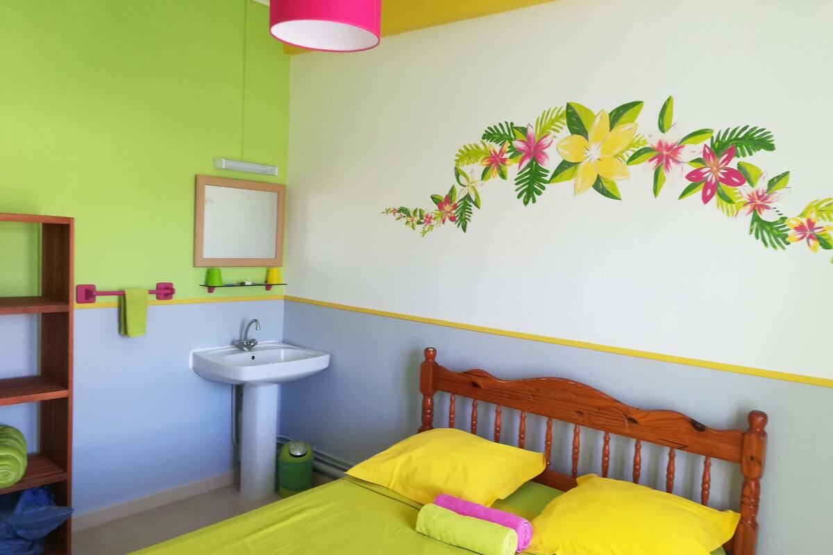 A bedroom with a bed, a wooden headboard, a bedside table, a mirror, and a wall-mounted sink.