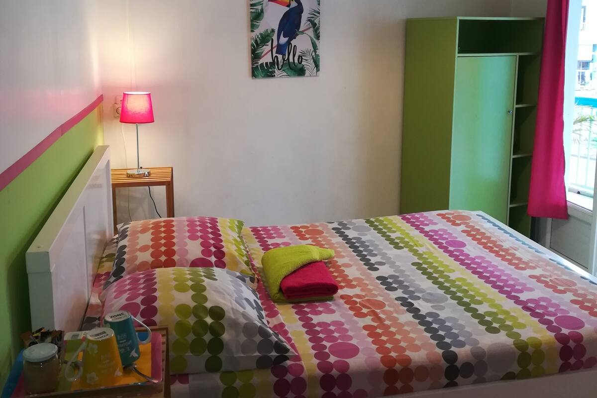 A bedroom with a bed, a nightstand, a lamp, a painting, a wardrobe, and an air conditioner.
