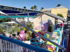 A balcony with colorful chairs and tables, a covered seating area, and a view of buildings and palm trees.