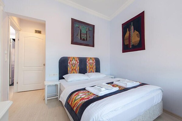 Una habitación de hotel con una cama, una mesita de noche, una puerta y dos cuadros en la pared.