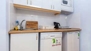 A compact kitchen with white cabinets, a wooden countertop, a microwave, a dishwasher, and a cutting board. - Hotel Sufi (Istanbul)