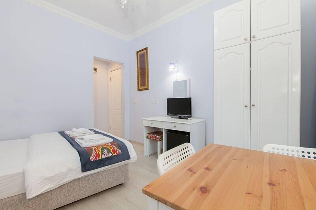 A bedroom with a bed, a desk with a computer, a TV, and a wardrobe.