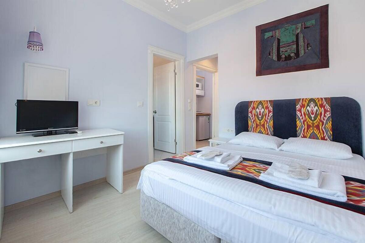 A bedroom with a bed, a desk, a television, and a door leading to a bathroom.