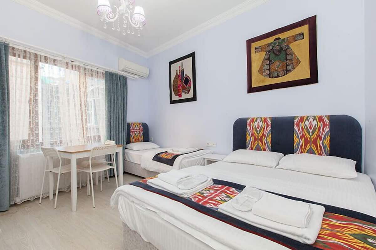 A hotel room with two beds, a desk, and a chair. There are two framed pictures on the wall.