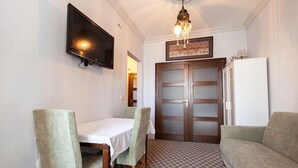 A room with a dining table, two chairs, a television, a wooden door, and a sofa. - Hotel Sufi (Istanbul)