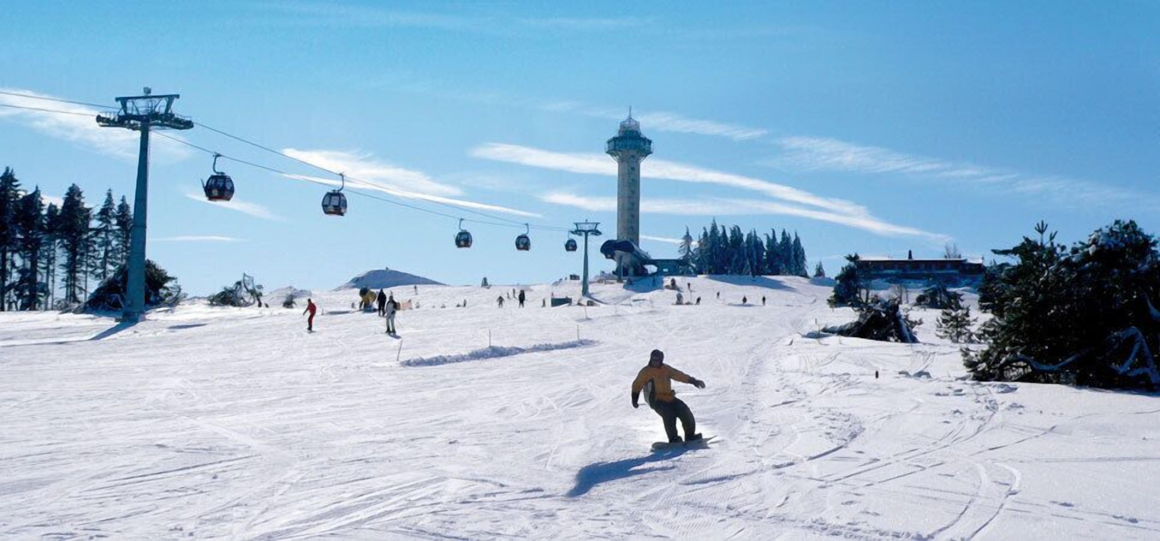 A snowy ski slope with a gondola lift, a tower, and a building in the background.