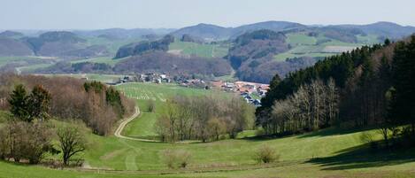 A rural landscape with rolling hills, a small village, and a winding road.