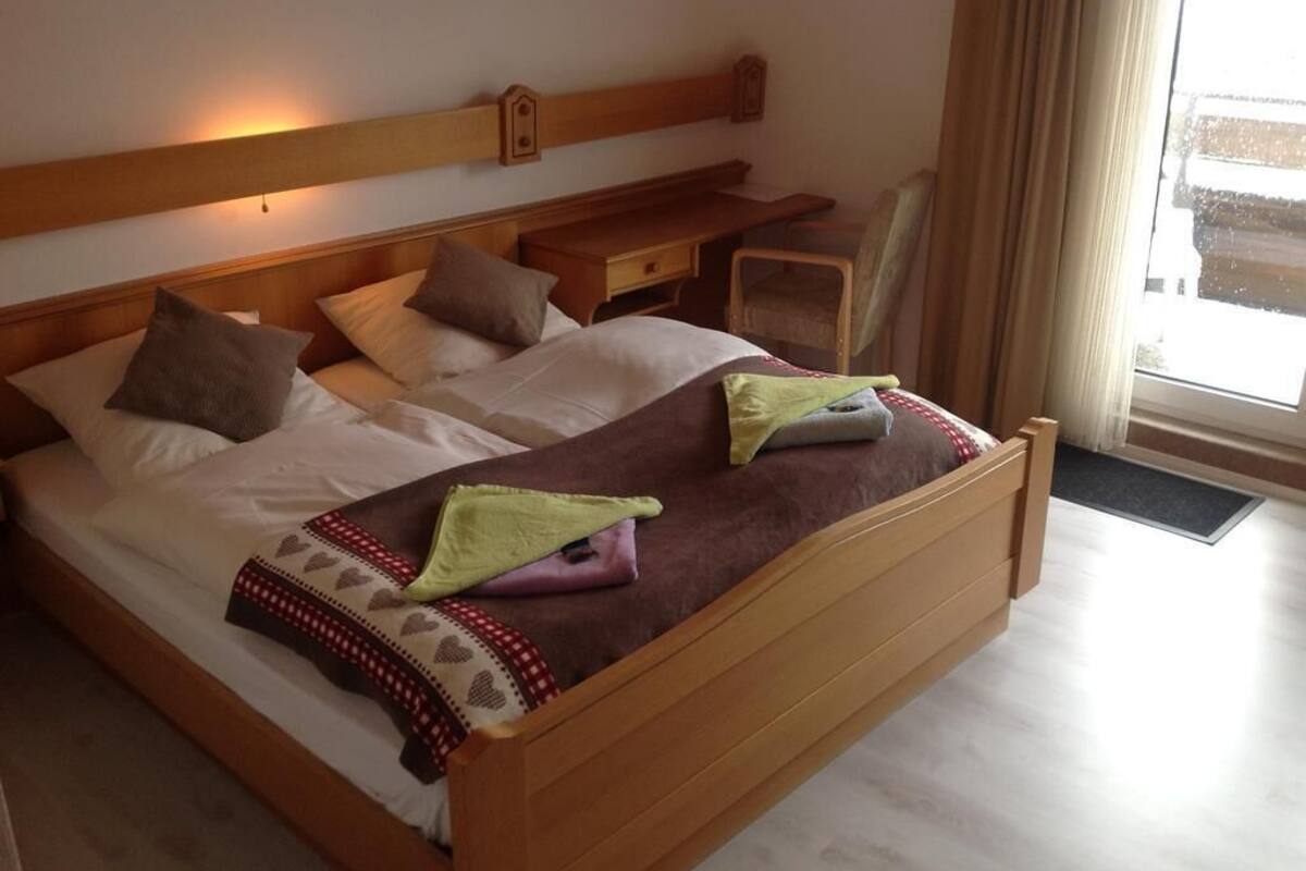 A neatly made bed with a wooden headboard, a bedside table, and a chair.