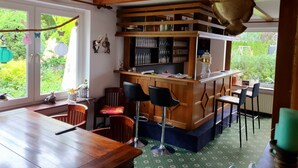 A cozy bar area with wooden furniture, a bar counter, and a view of greenery outside. - Pension Robin Hood (Willingen)