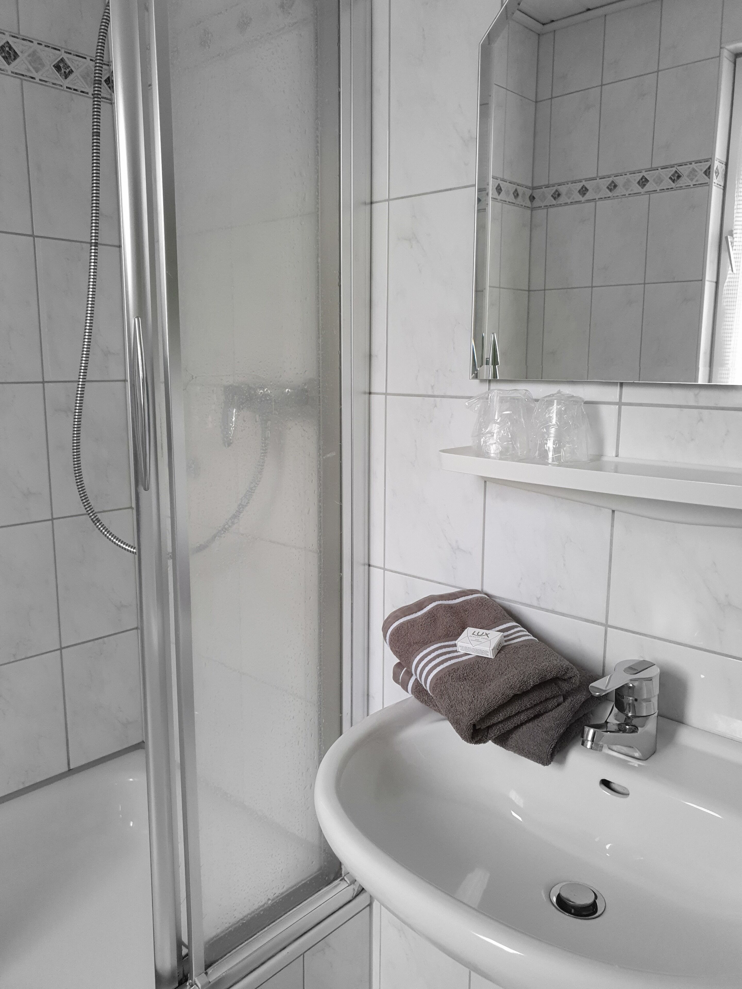 Un baño con ducha de vidrio, un lavabo blanco y un espejo encima.