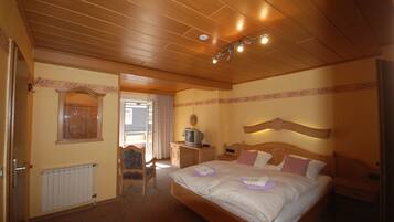 A bedroom with a wooden ceiling, a bed with white bedding, a nightstand, a television, and a radiator.
