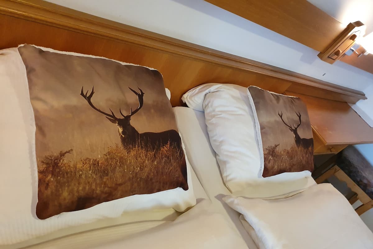 A hotel room with two beds, each with a pillow featuring a deer silhouette.