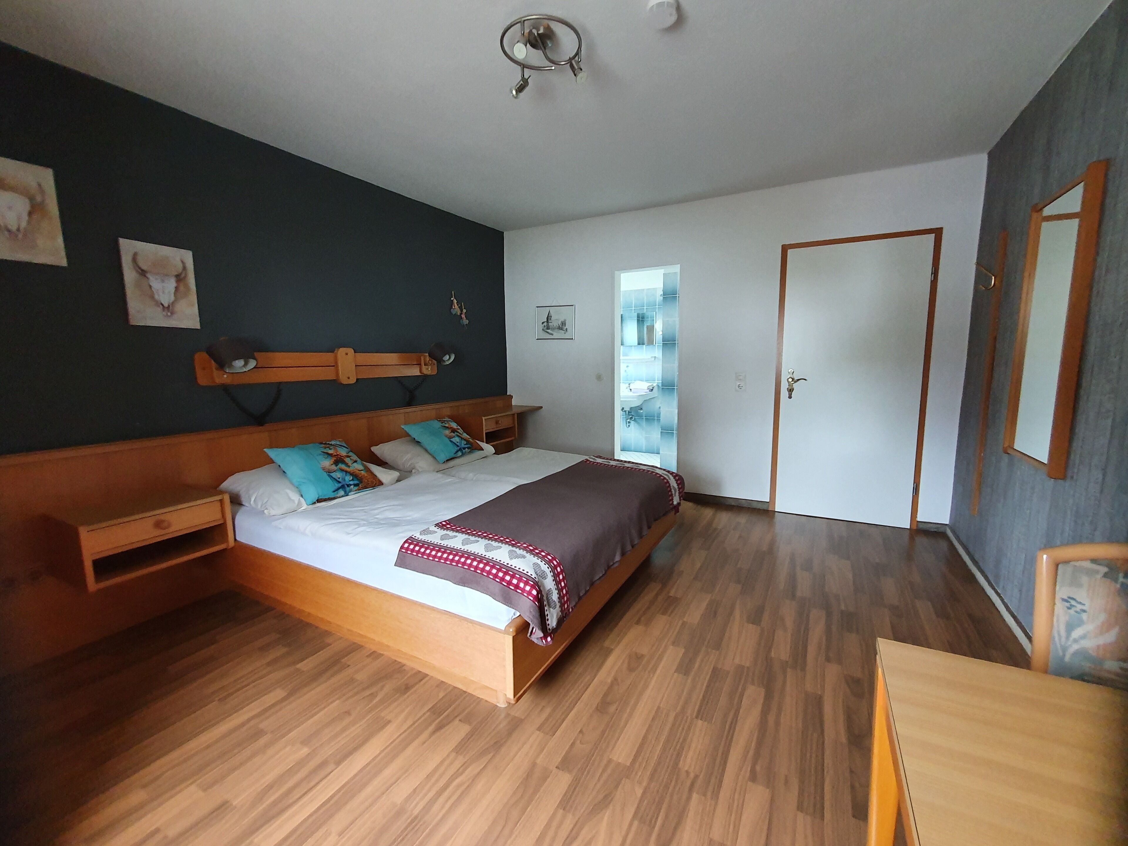 A bedroom with a wooden bed, a nightstand, a bedside table, a mirror, and a door.