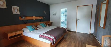 A bedroom with a wooden bed, a nightstand, a bedside table, a mirror, and a door.