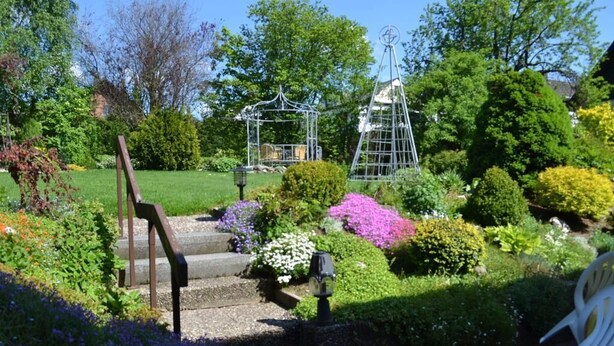 A garden with a gazebo, a metal sculpture, and a chair. - Pension Robin Hood (Willingen)