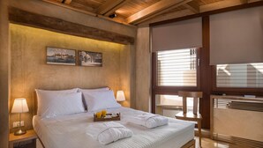 Quarto de hotel com uma cama grande, duas luminárias de cabeceira, uma bandeja com toalhas e suco, e vista para o exterior pela janela.