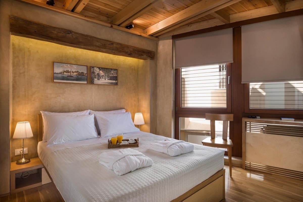 A hotel room with a large bed, two bedside lamps, a tray with towels and juice, and a view of the outside through a window.