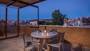Um terraço no telhado com uma mesa redonda, cadeiras e uma garrafa de vinho.