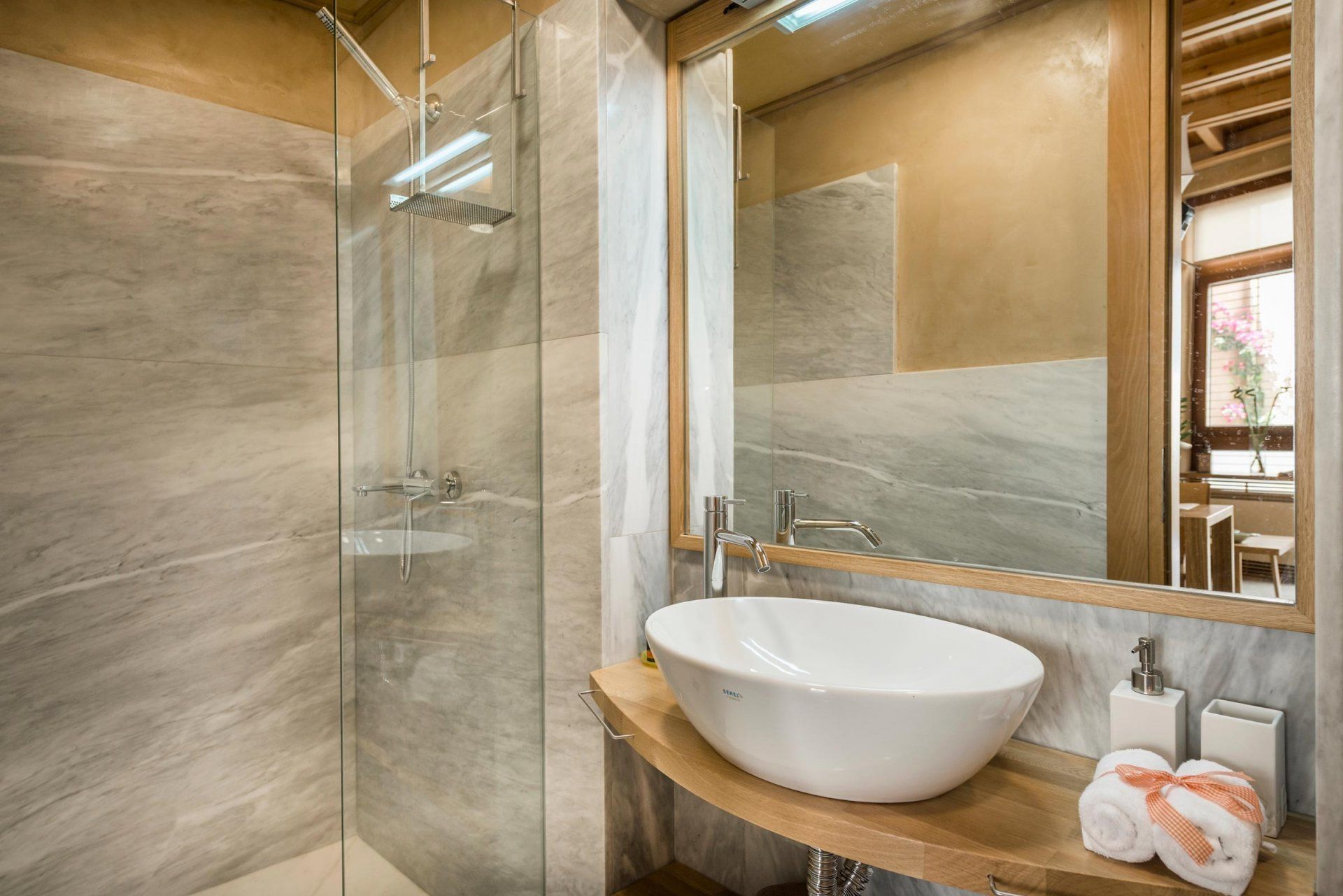 Une salle de bain moderne avec une douche à parois de verre, un grand miroir et un lavabo sur colonne blanc.