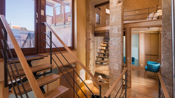 Interior moderno com escada de madeira, parede de vidro e vista exterior.