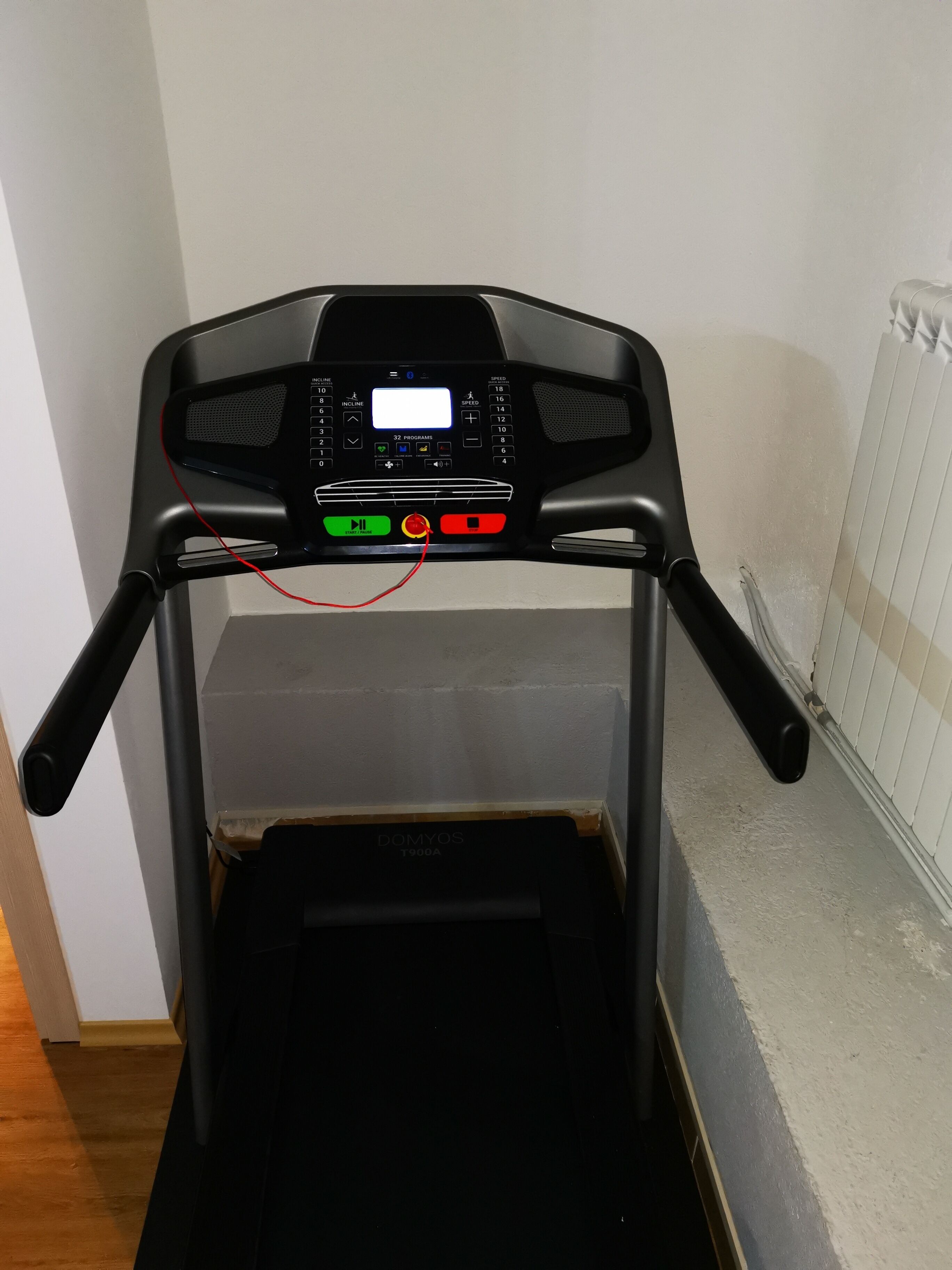 Una cinta de correr con pantalla digital, botones de control y un cable rojo.