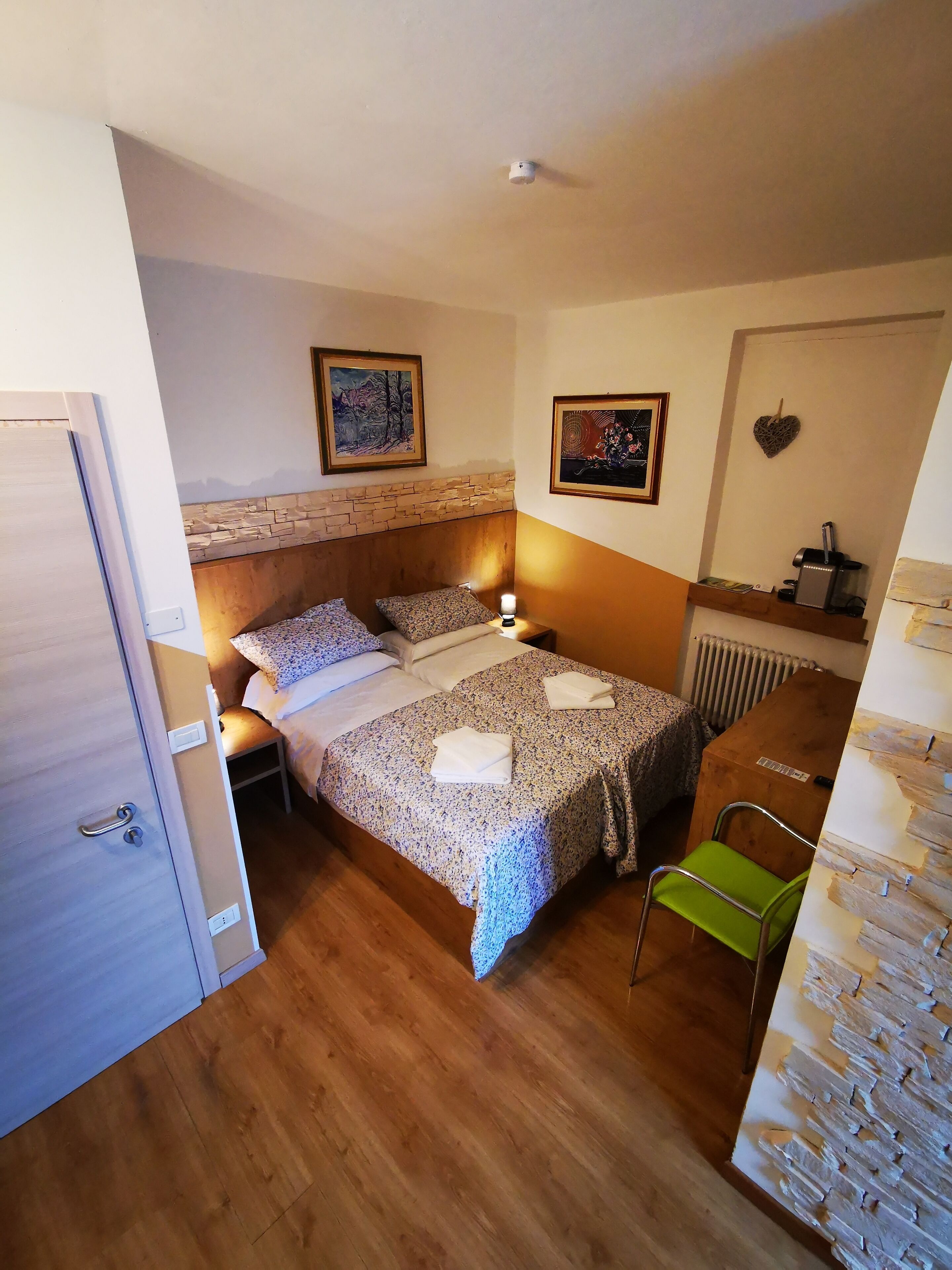 Ein Schlafzimmer mit einem Holzbett, zwei Nachttischen mit Lampen, einem Heizkörper, einem grünen Sessel und einer Tür.