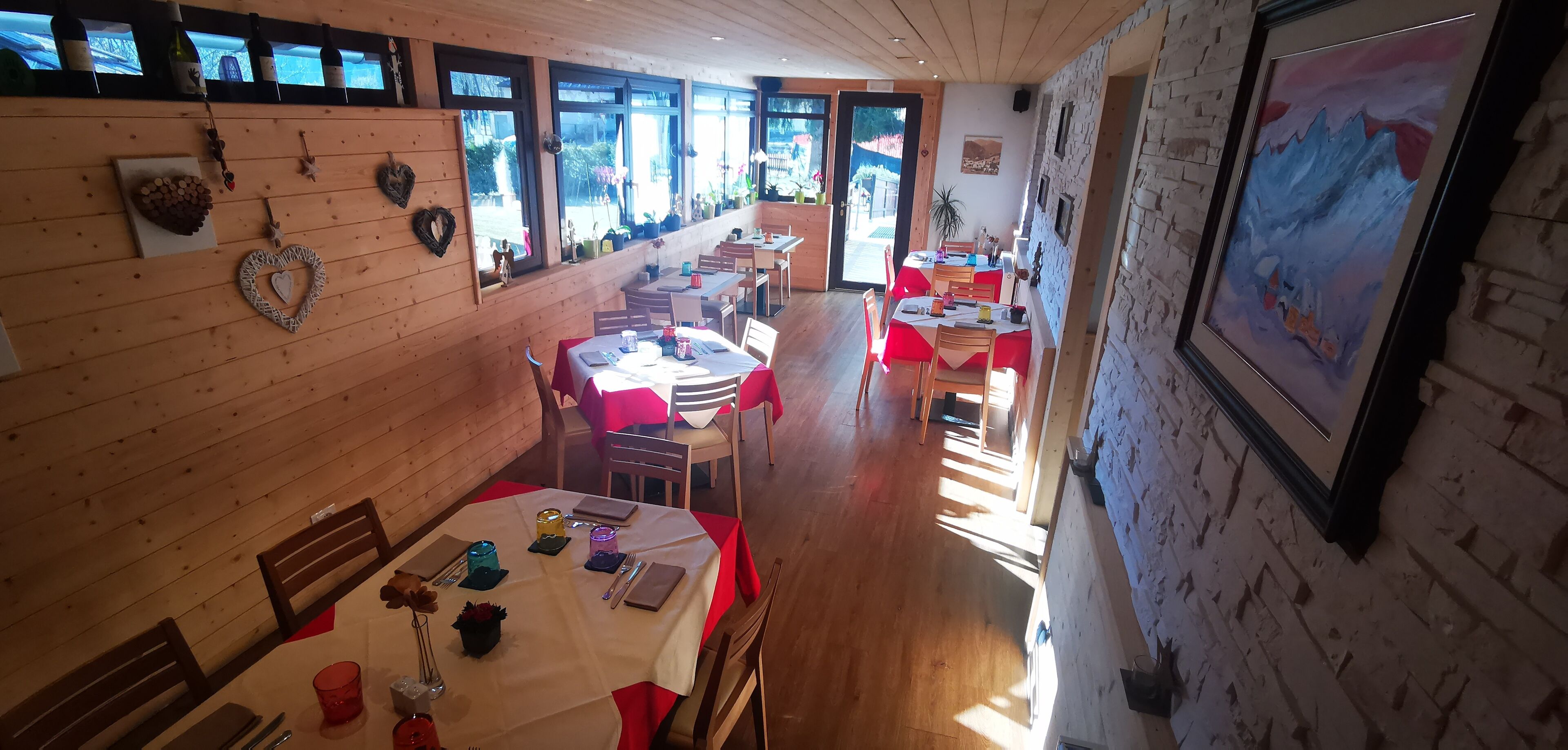 Un restaurant aux murs en bois et aux grandes fenêtres, avec des tables recouvertes de nappes rouges et une variété de plats proposés.