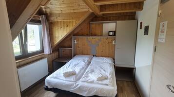 Une chambre avec un plafond en bois, un lit recouvert de draps blancs, une petite table et un radiateur.