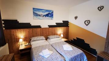 A double room with two beds, wooden headboard, bedside lamps, a painting on the wall, and heart-shaped decorations.