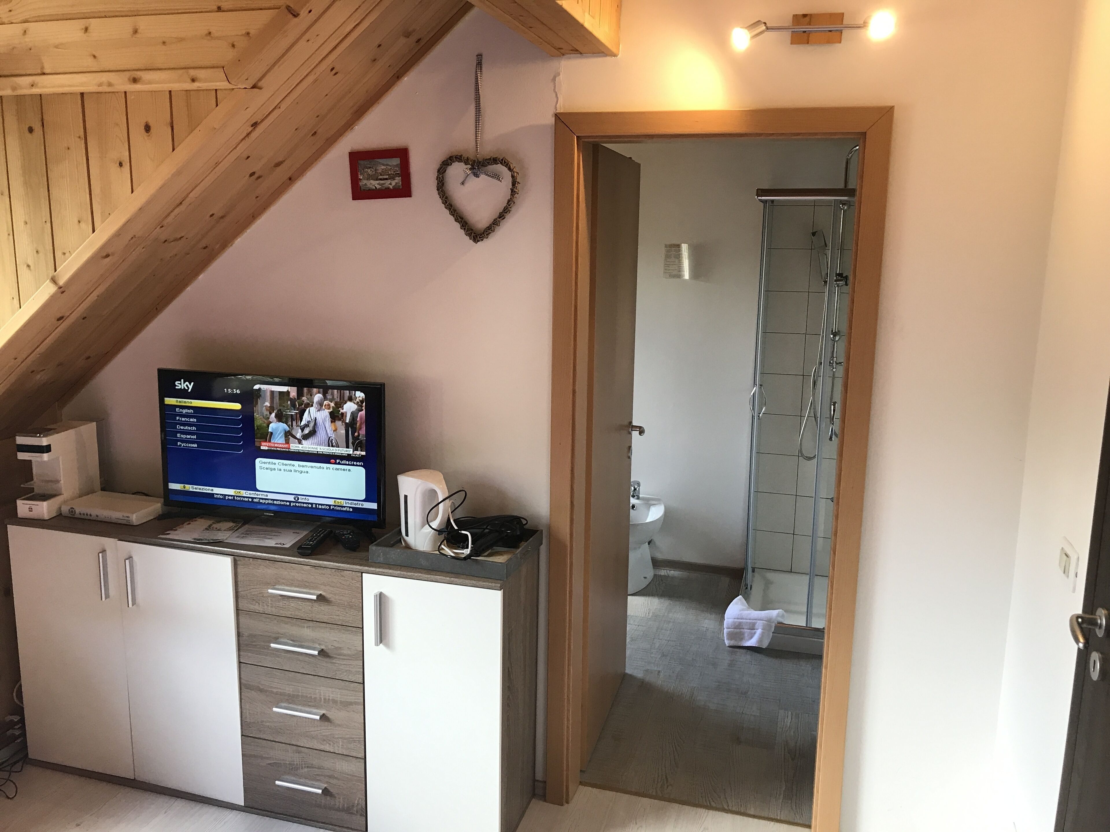 A room with a wooden ceiling, a television displaying a news channel, a heart-shaped decoration, and a shower area.