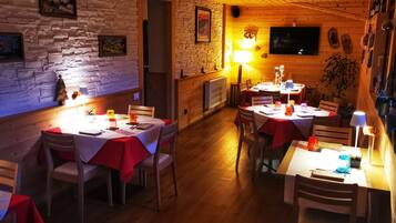 Ein gemütliches Restaurant mit Holzwänden und Steindetails, mit mehreren Tischen mit roten Tischdecken und Kerzen.