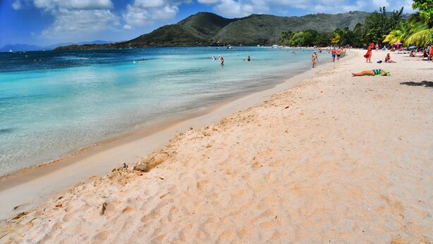 A beach with clear turquoise water, sandy shore, and people enjoying the beach. - Airstream Paradise (Sainte-Anne)