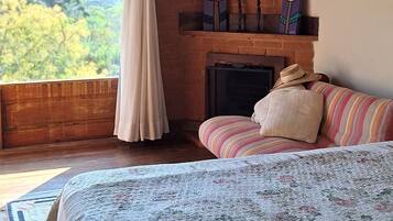 A bedroom with a bed, a fireplace, a view of the mountains, and a hanging light fixture.