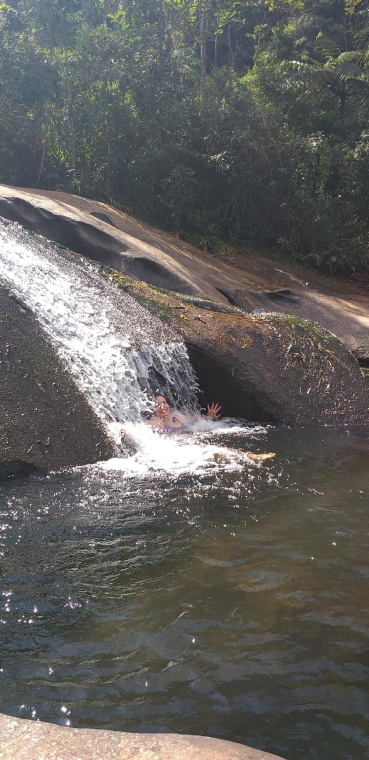 Uma cascata despencando sobre um afloramento rochoso em direção a um lago, rodeado por vegetação densa.