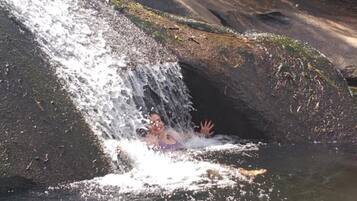 Uma cascata despencando sobre um afloramento rochoso em direção a um lago, rodeado por vegetação densa.