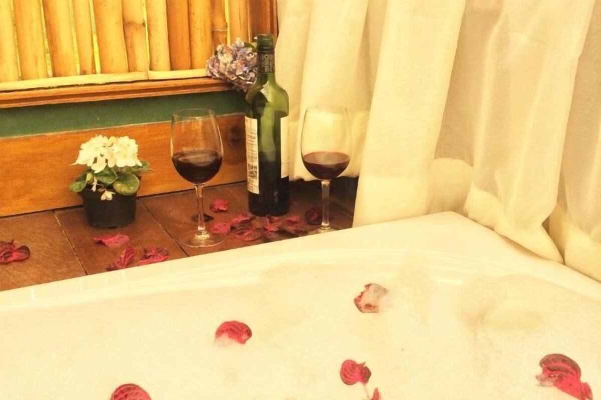 Eine Wanne mit Rosenblättern, eine Weinflasche und zwei Weingläser auf einem Holzboden.