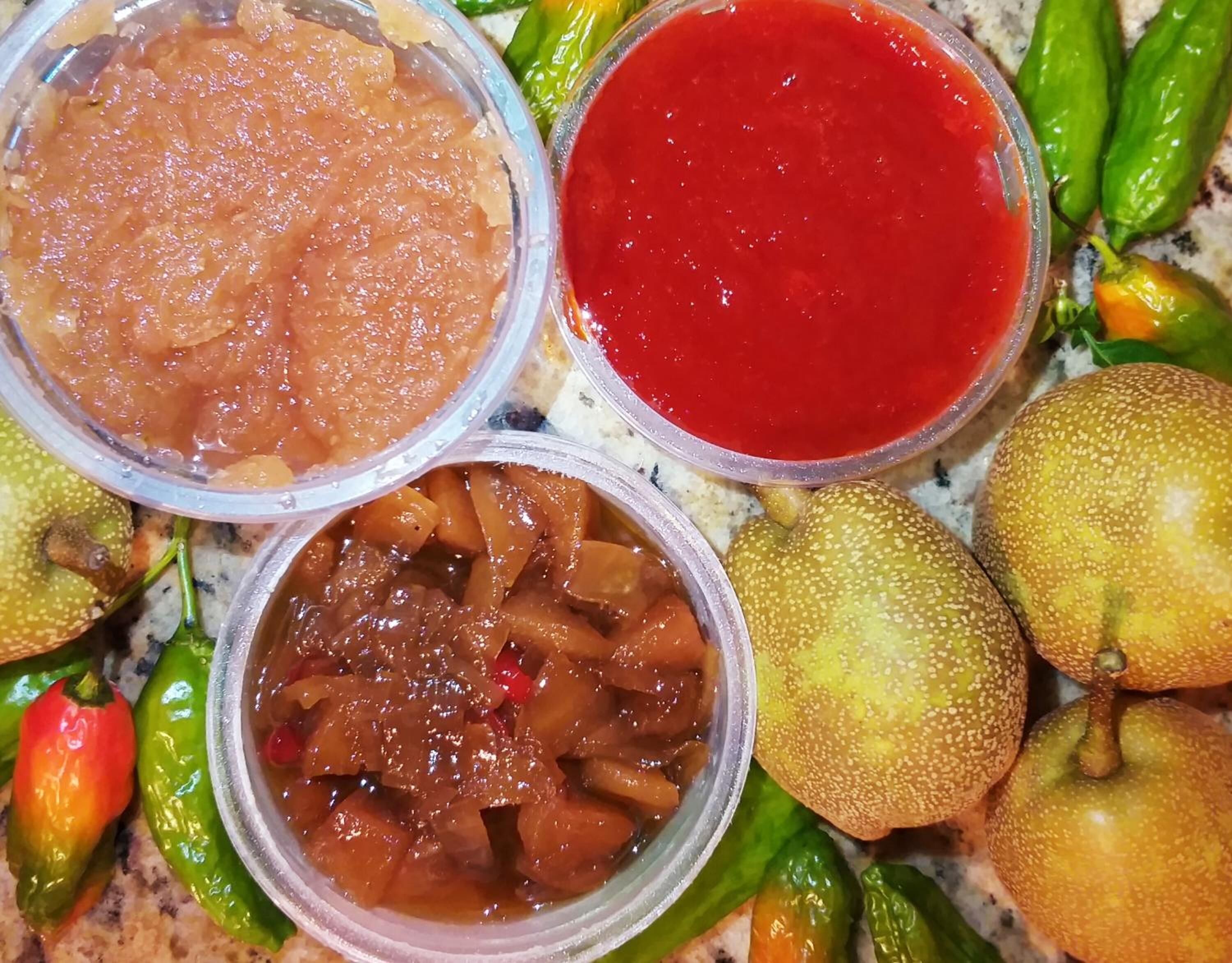 Tres recipientes de comida con diferentes salsas y varias frutas y verduras enteras.