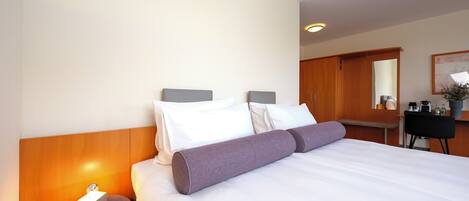 A hotel room with a bed, bedside table, lamp, and a desk with a chair.